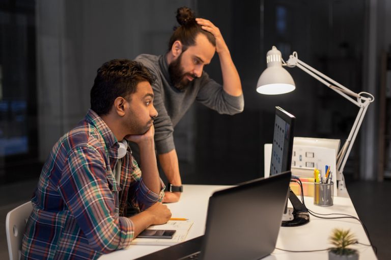 Technology problems concept. Men with hand on head working at desk in dark office.